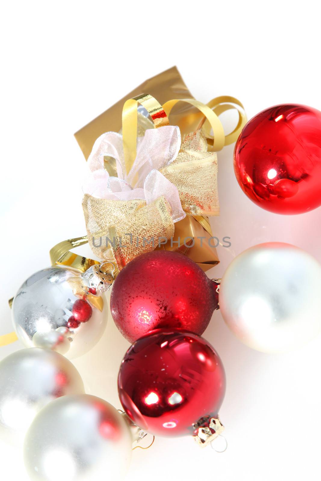 Decorative gold Christmas gift with and ornamental ribbon amongst scattered red and white baubles for a colourful seasonal background with copyspace for your xmas wishes