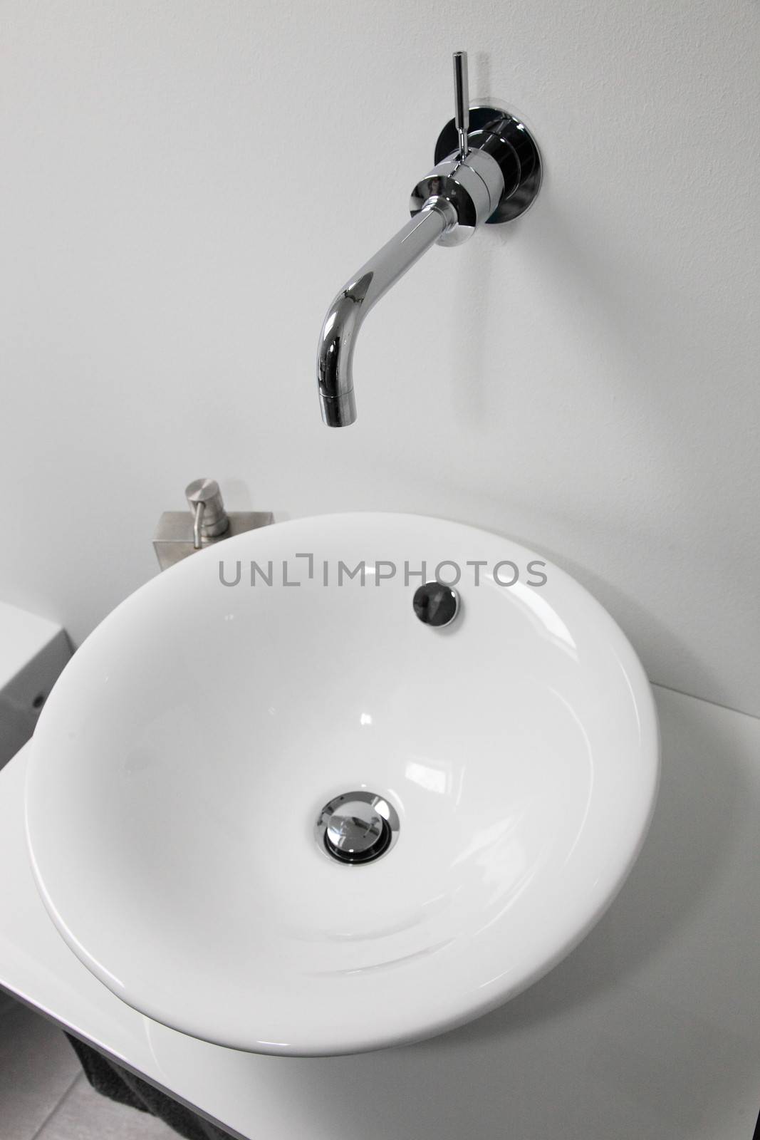 Modern ceramic bowl-shaped handbasin and wall mounted chrome tap in a contemporary bathroom or restroom