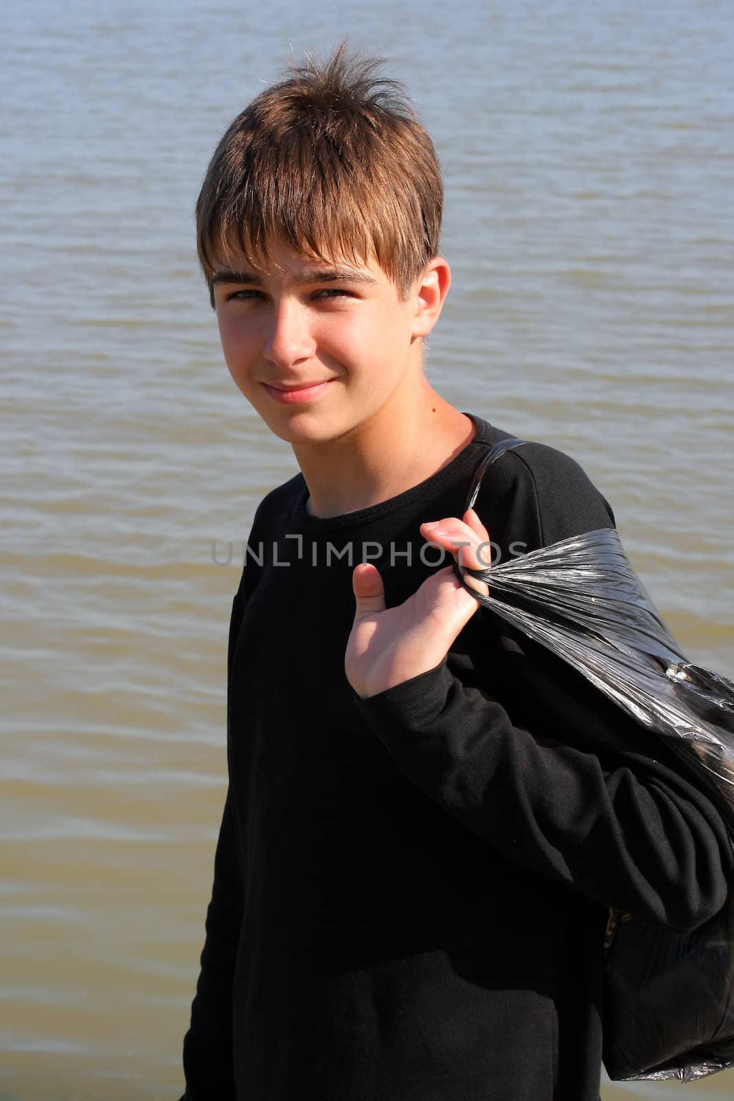 smiling boy stand near the water with a bag