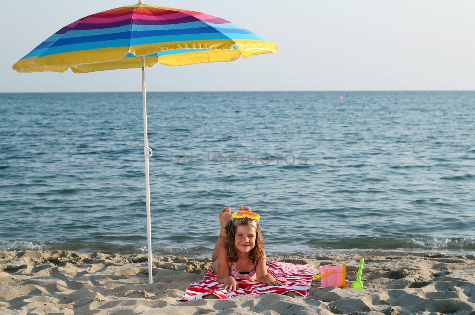 little girl with diving mask lying under sunshade on beach