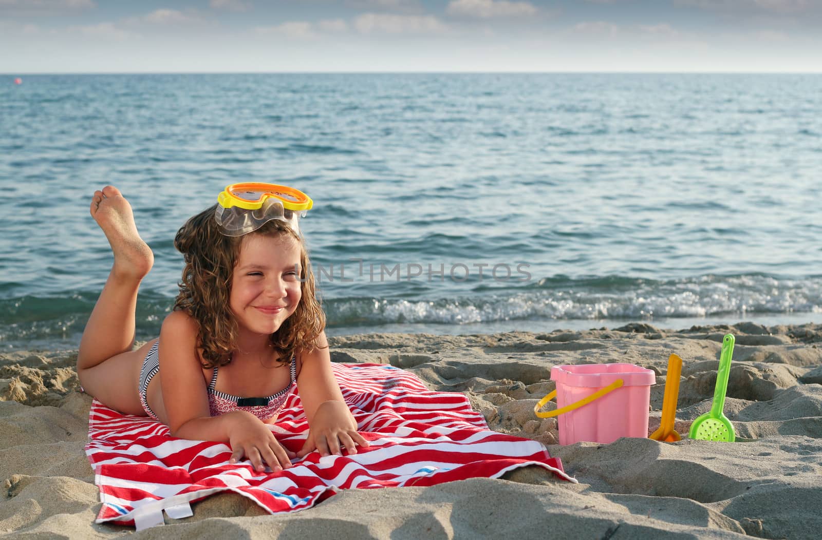 happy little girl with diving mask lying on beach by goce