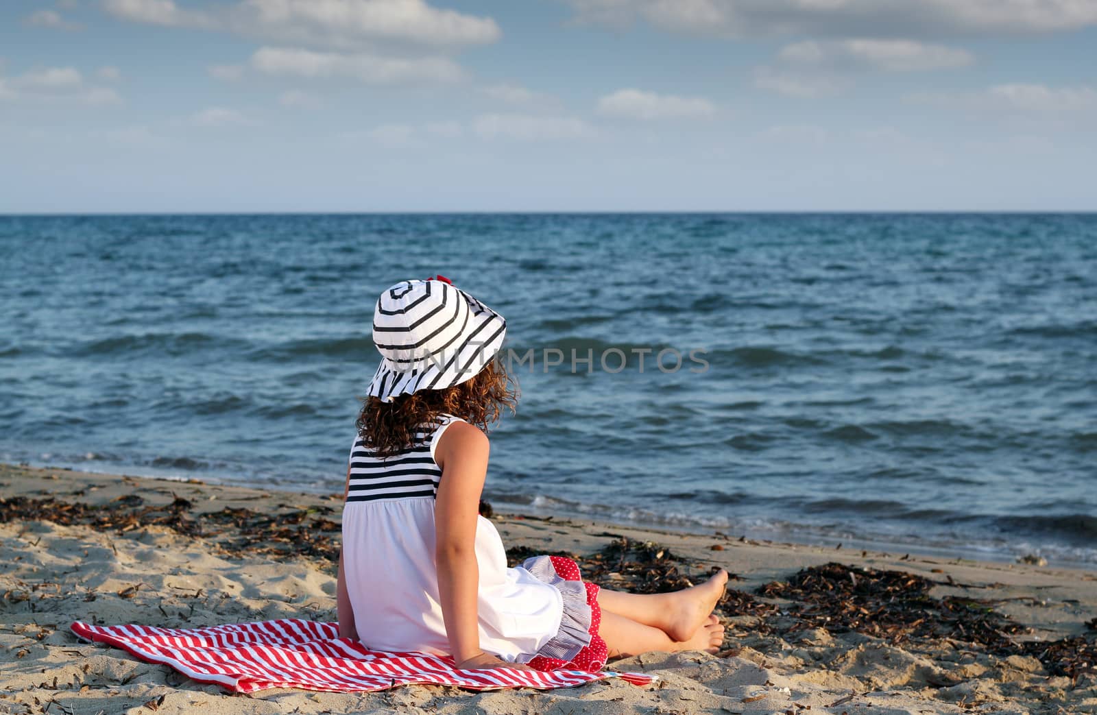 little girl sitting on beach by goce