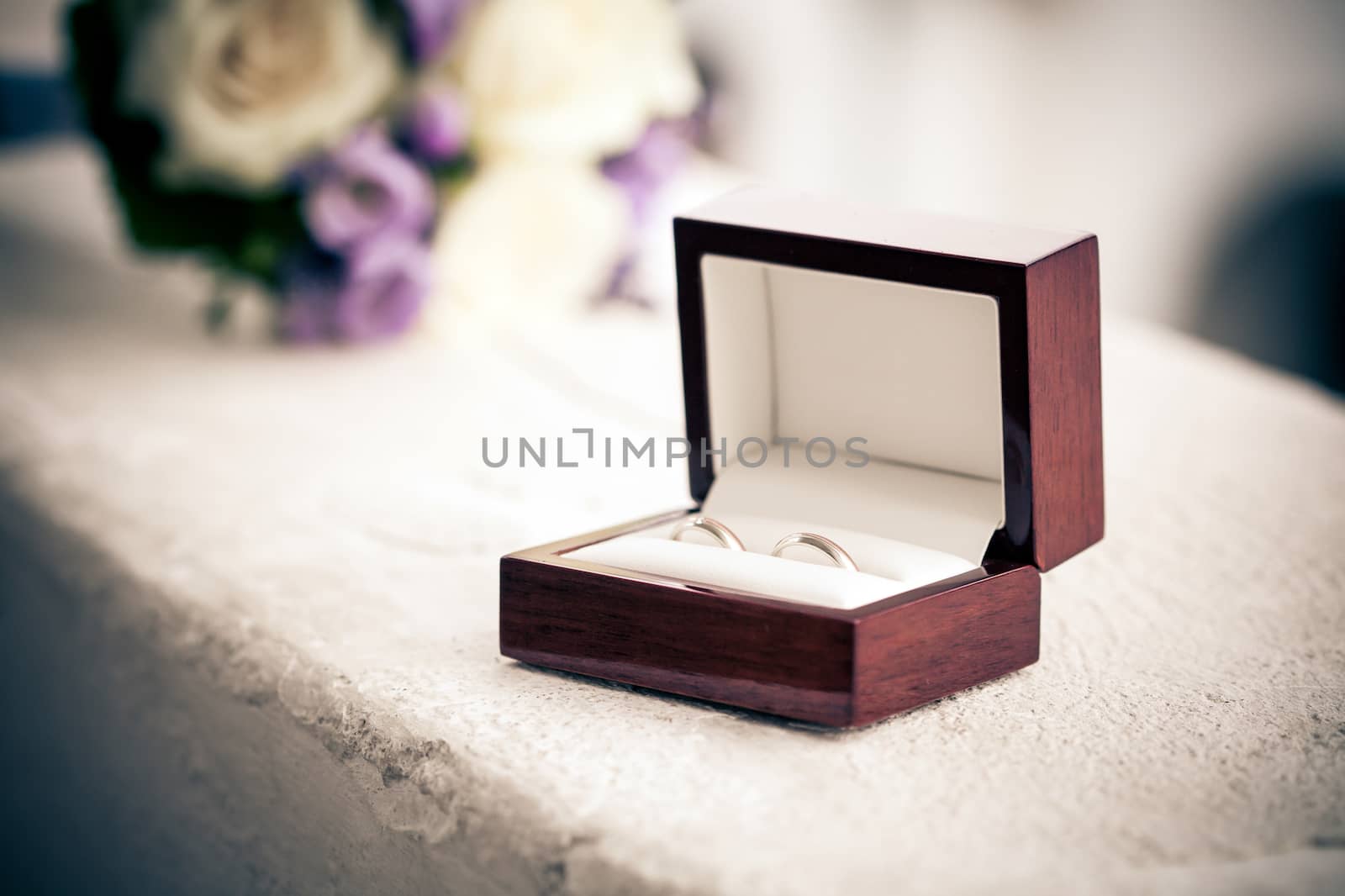 Wedding rings in a box with blurred bouquet on background