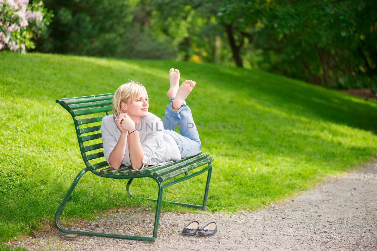 Young woman laying on bench in park and smiling