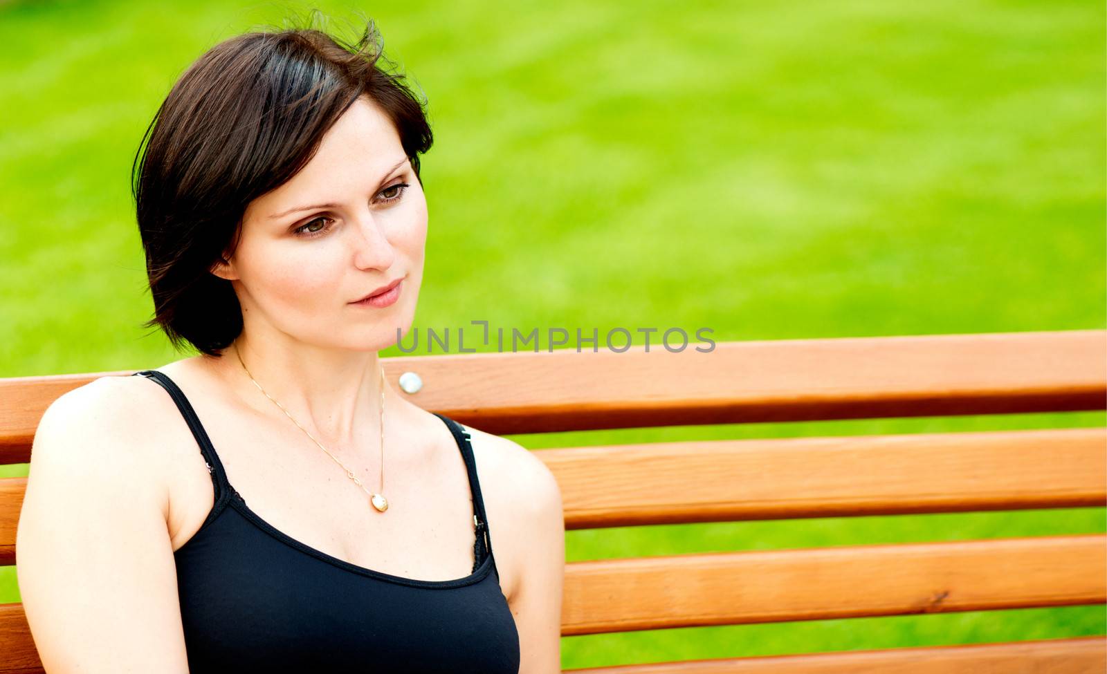 Sad brunette woman sitting on a bench against spring green bokeh background