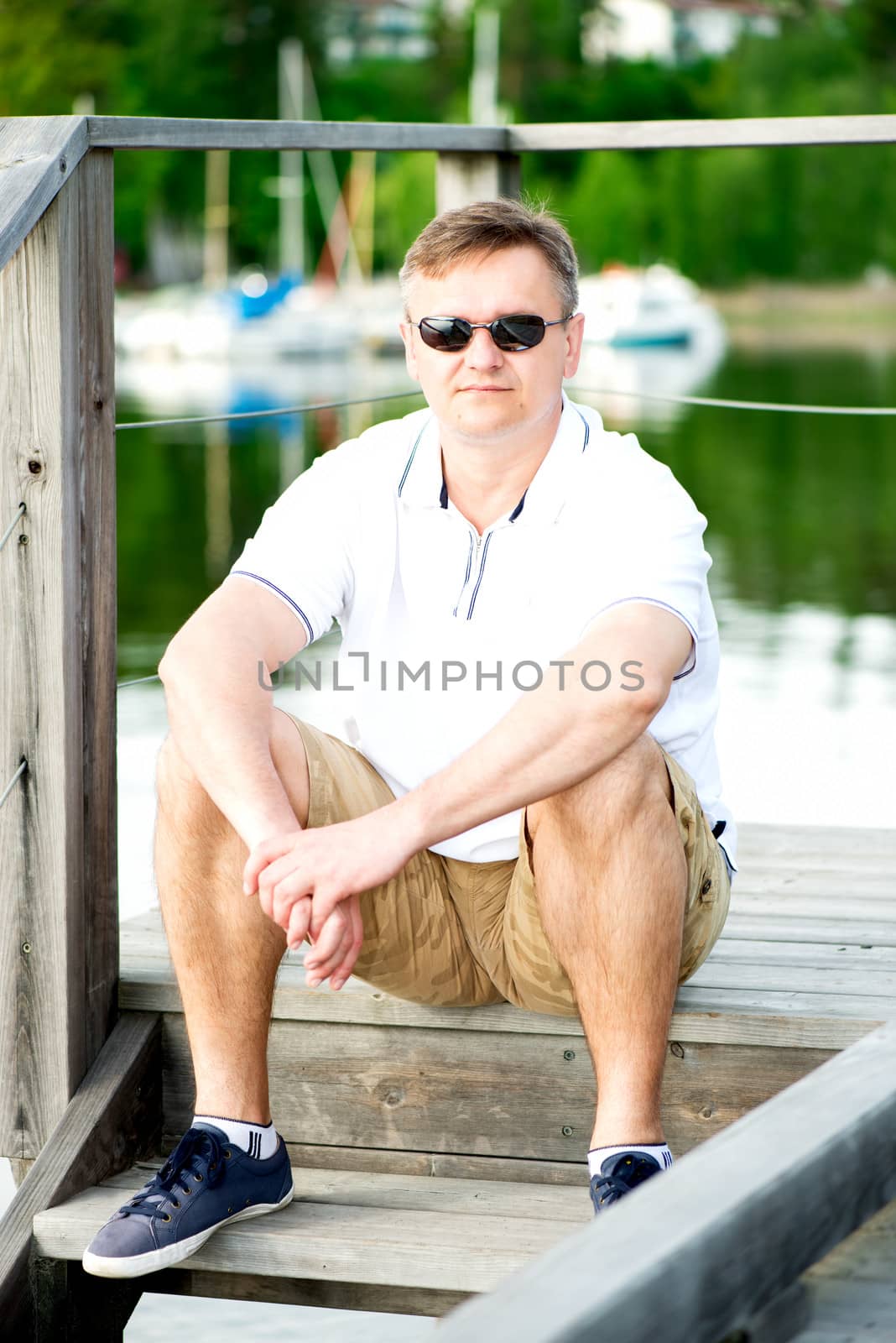 Mature man with sunglasses sitting at pier by Nanisimova