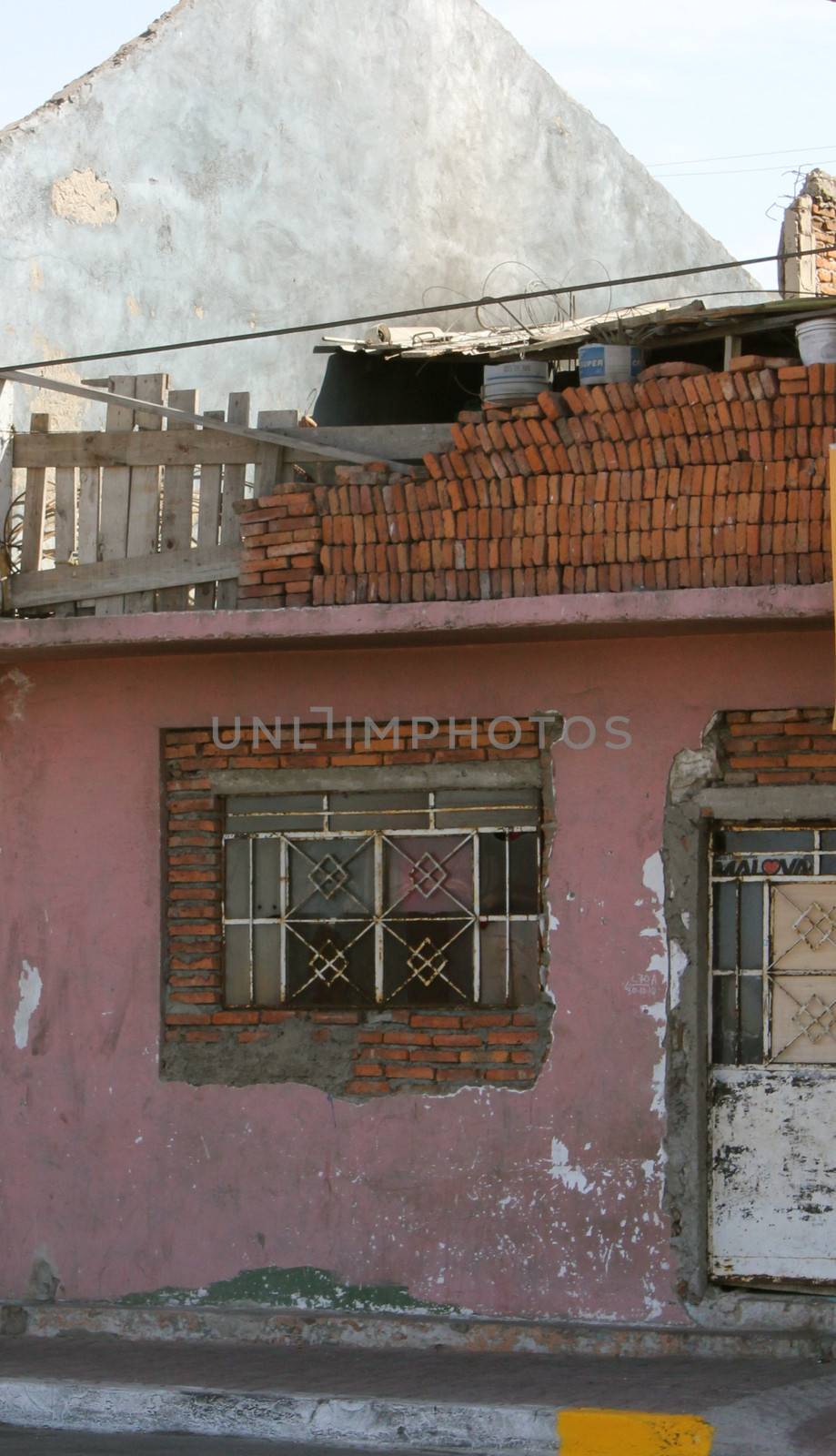 The exterior of an abandoned and decaying pink house with building materials on the rooftop, suggesting repairs.