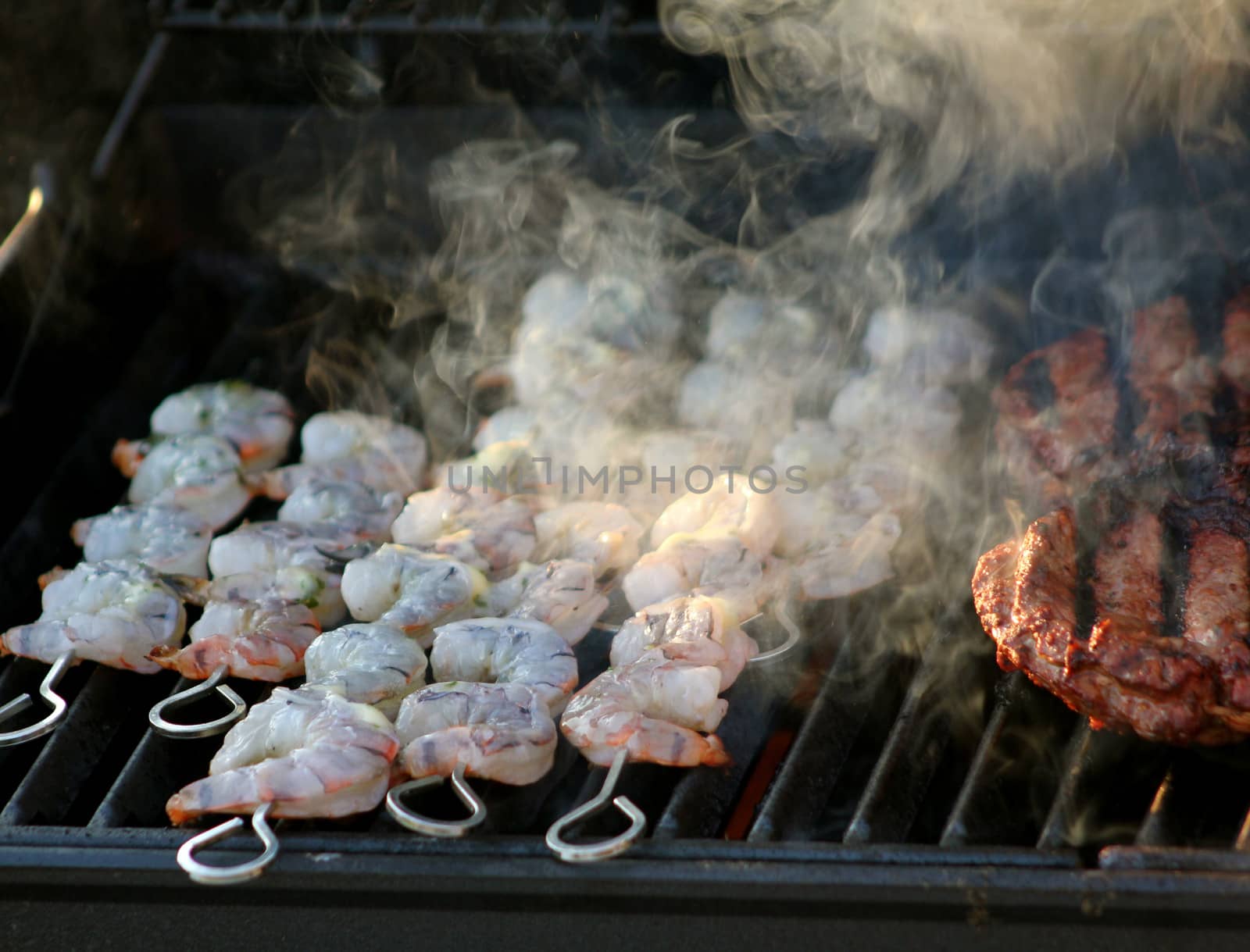 Skewered shrimp cooking (and smoking) on a barbecue grill along side beef