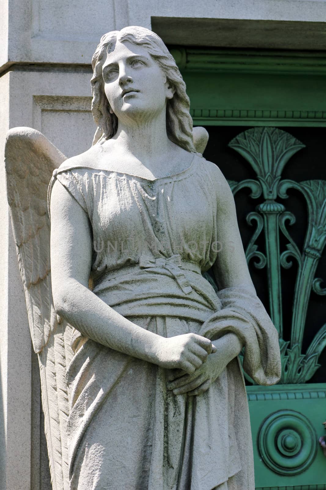 A stone statue of a young female angel guards the green weathered door to a mausoleum at Graceland Cemetery, Chicago, Illinois, USA