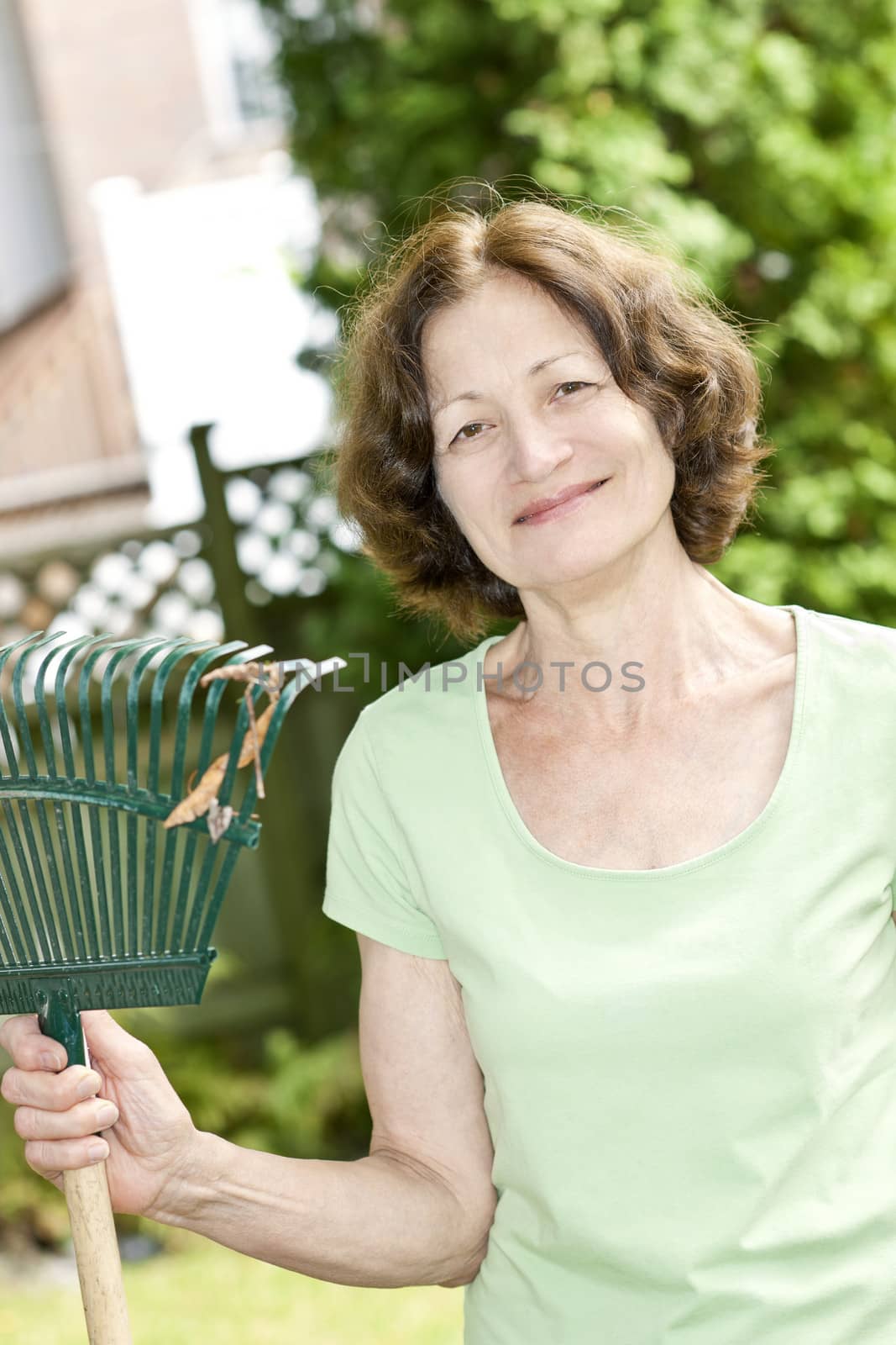 Senior woman smiling holding rake and gardening outside