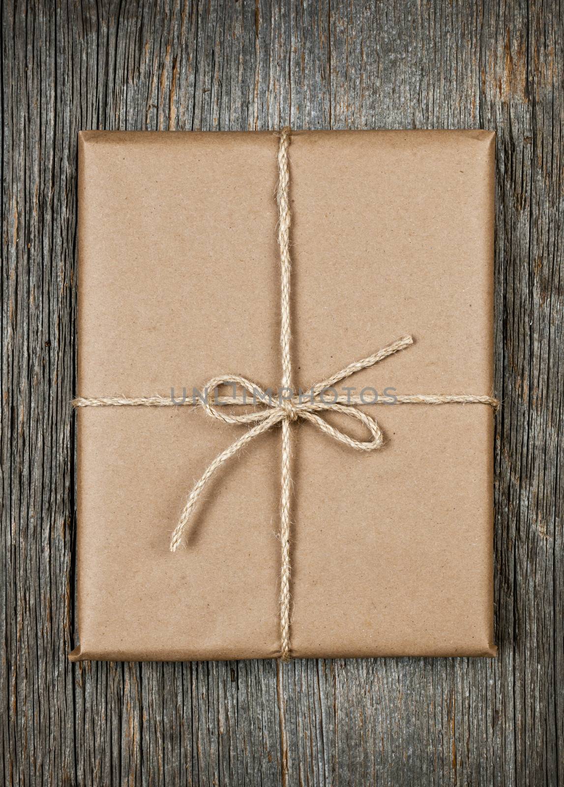 Gift package in brown paper wrapper tied with string on rustic wood background