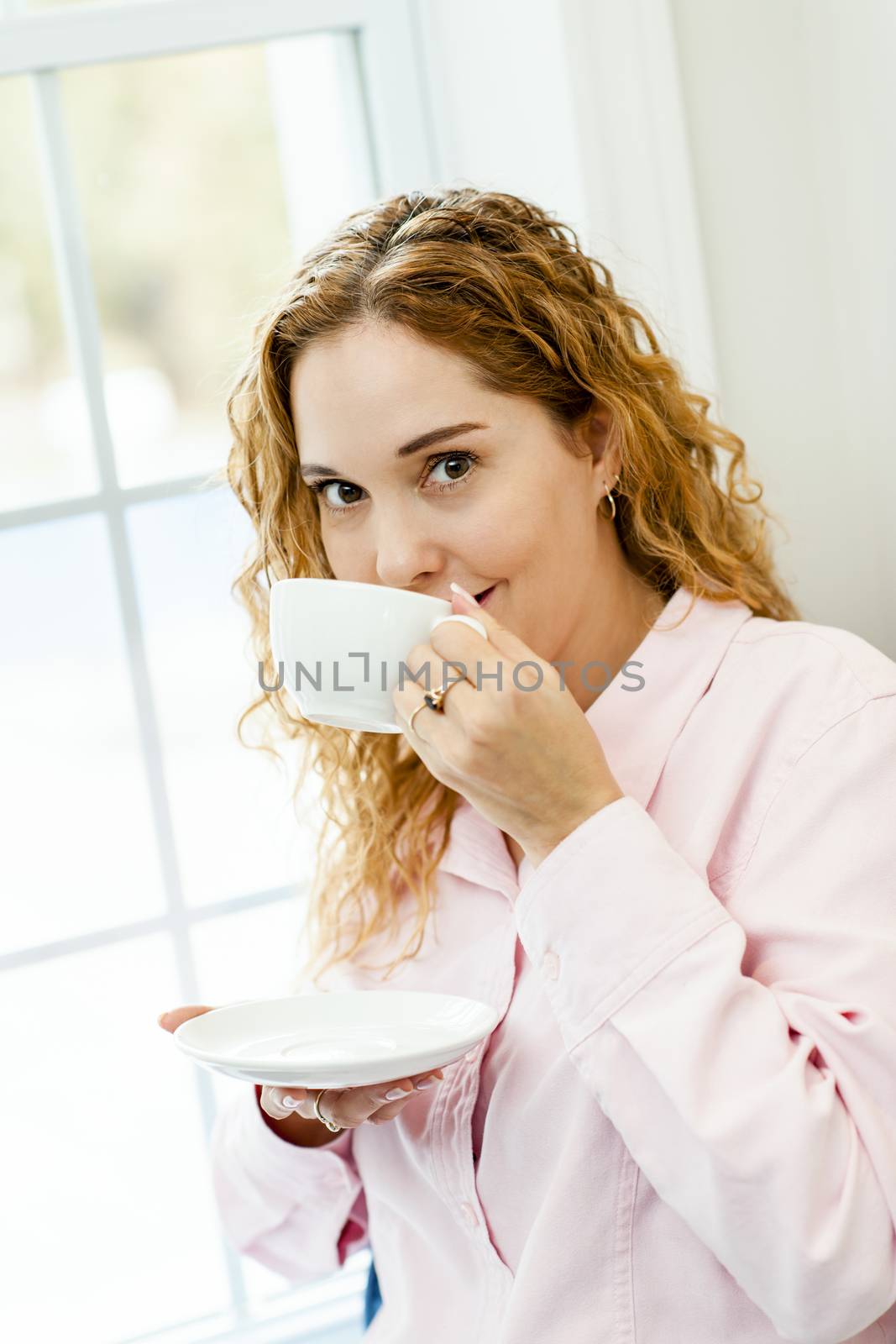 Smiling caucasian woman relaxing by window holding cup of coffee