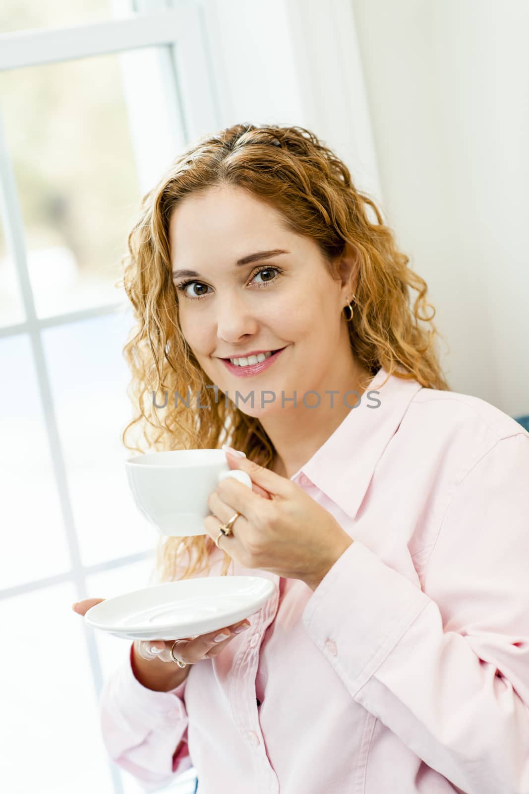 Smiling caucasian woman relaxing by window holding cup of coffee