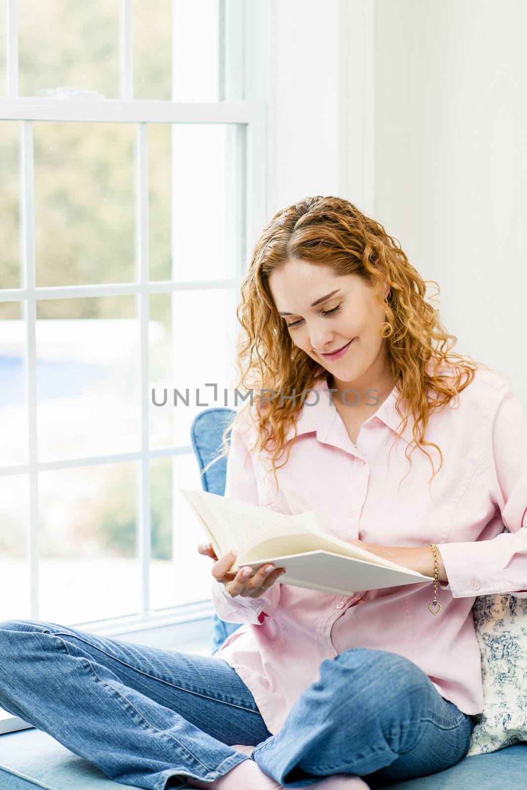 Smiling caucasian woman reading book by window at home