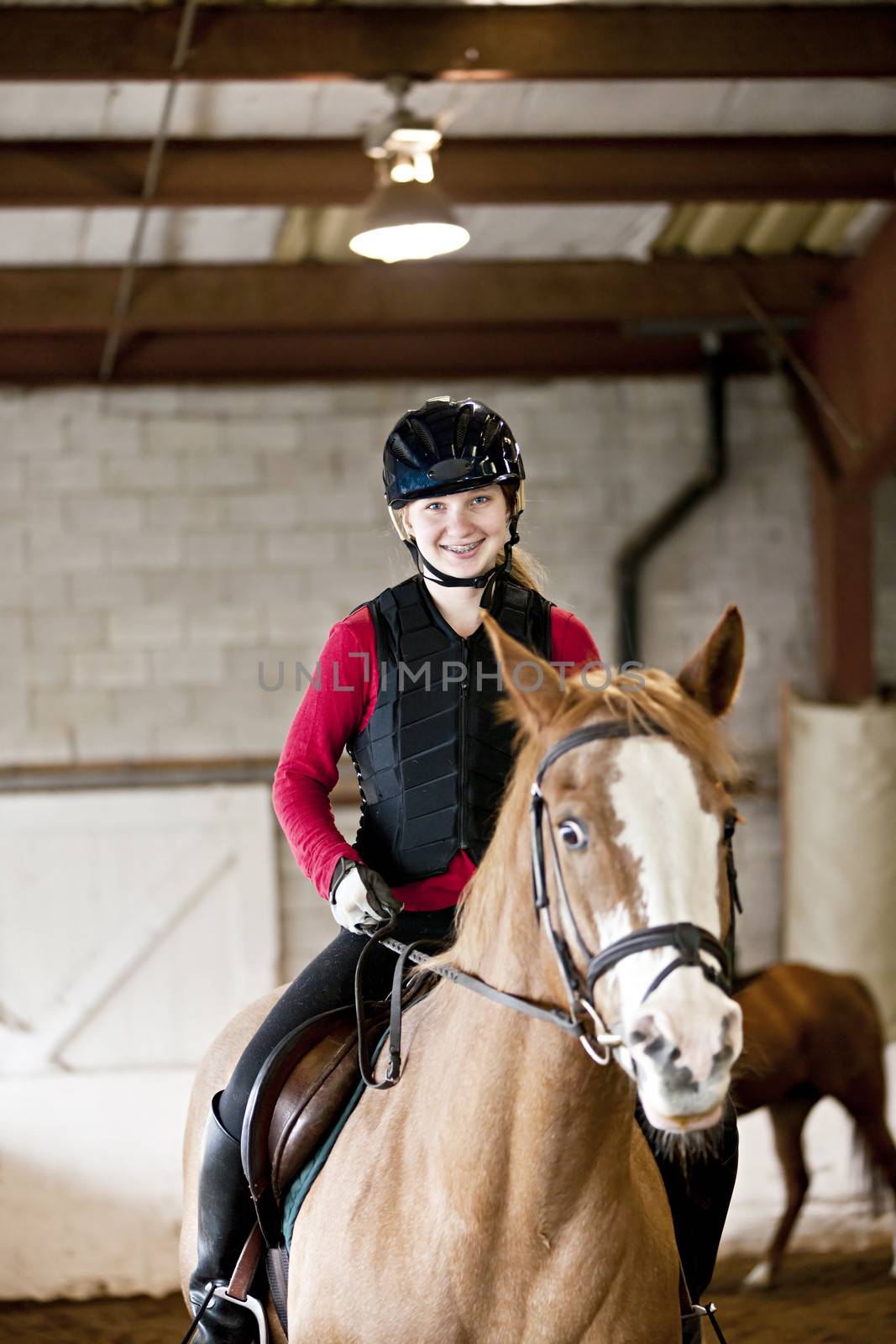 Teenage girl on horseback wearing helmet and safety vest in indoor arena