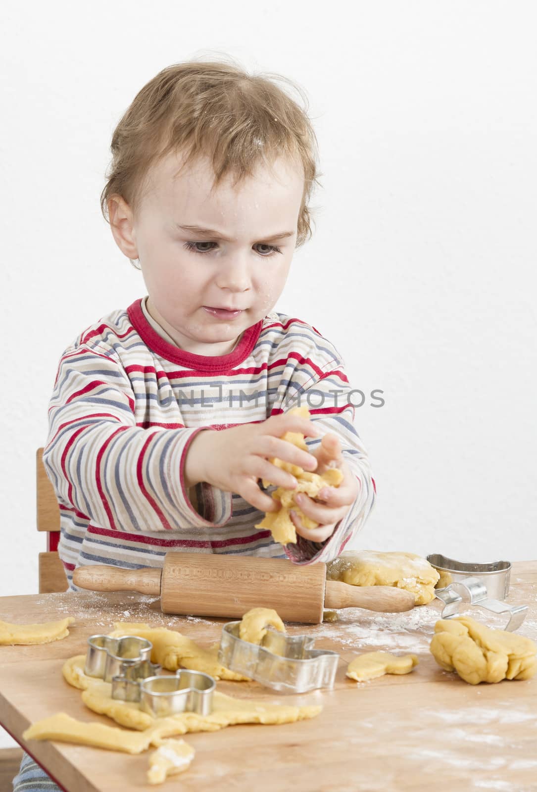young child in vertical image looking at baking tools and working with dough