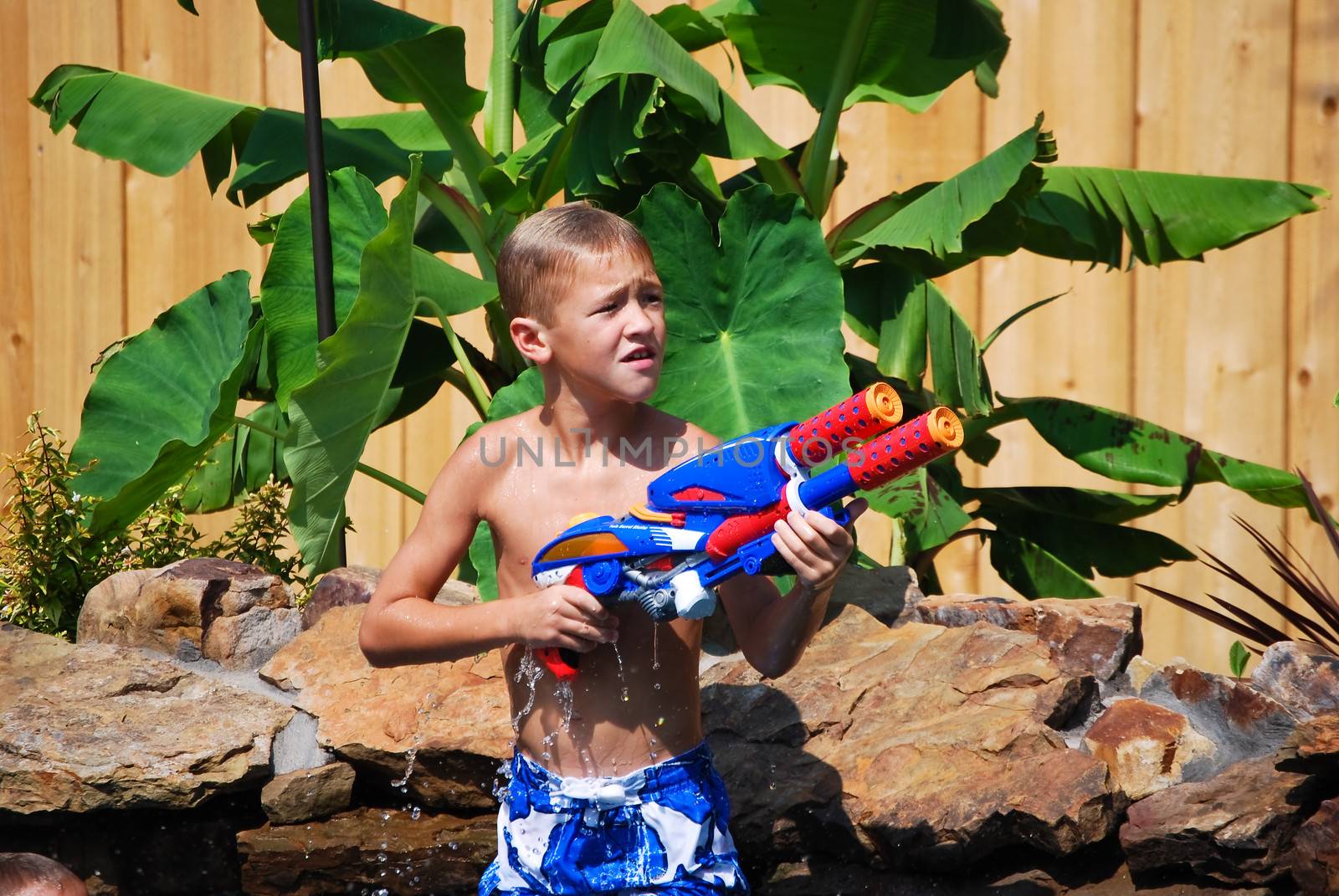 Cute young boy in swimming pool with water gun.