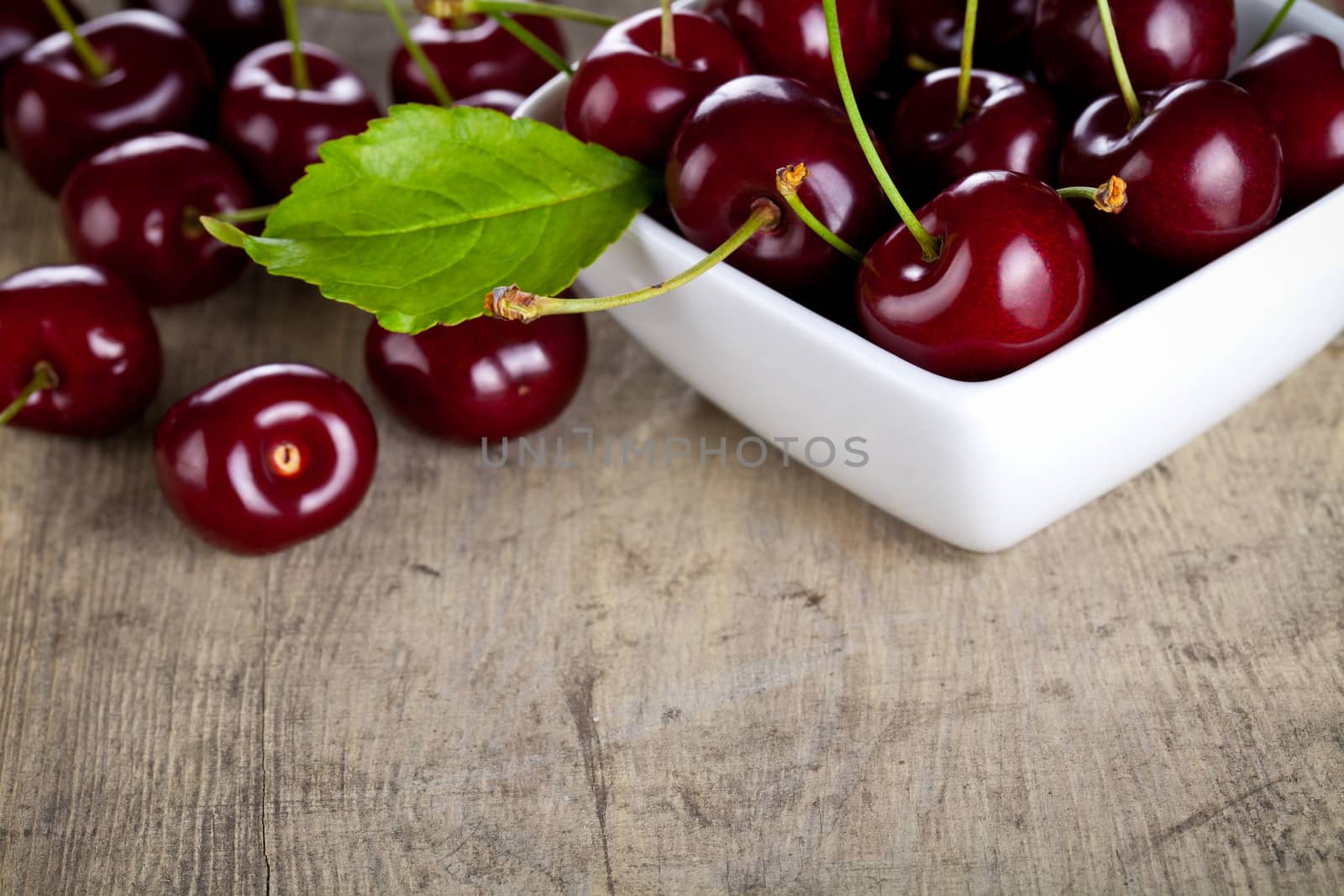 Cherries in white bowl on wooden table background. Copy space. Macro shot