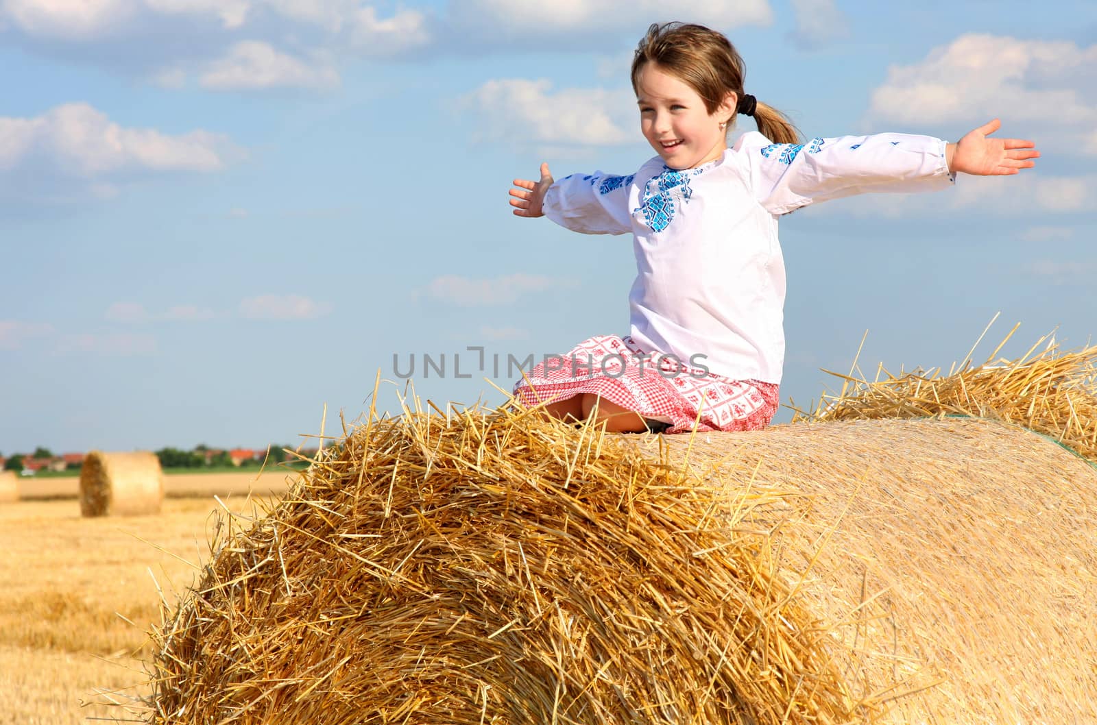 small rural girl on the straw after harvest field with straw bales