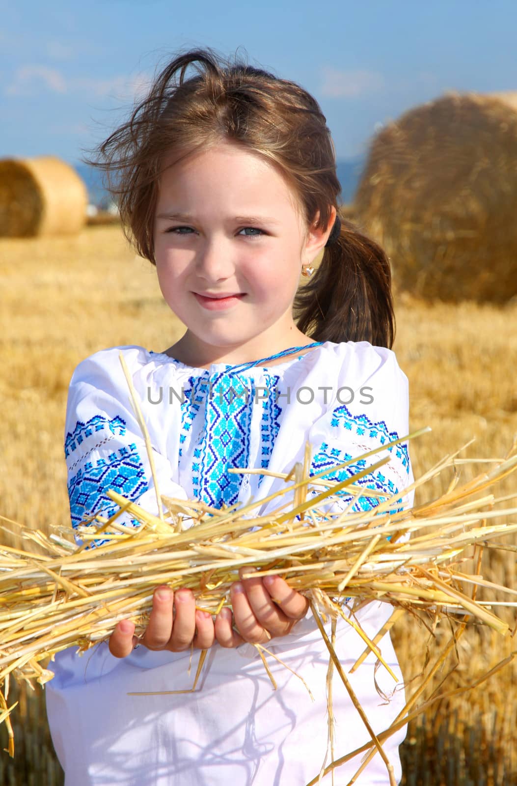 small rural girl on harvest field with straw bales