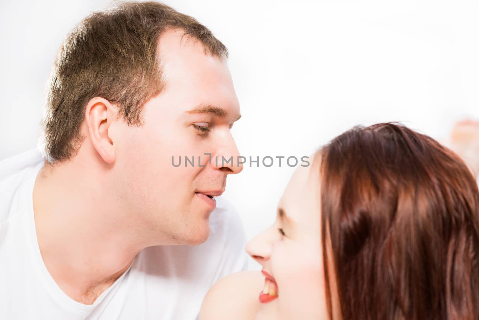 Young man and woman lying together in bed, smiling and happy