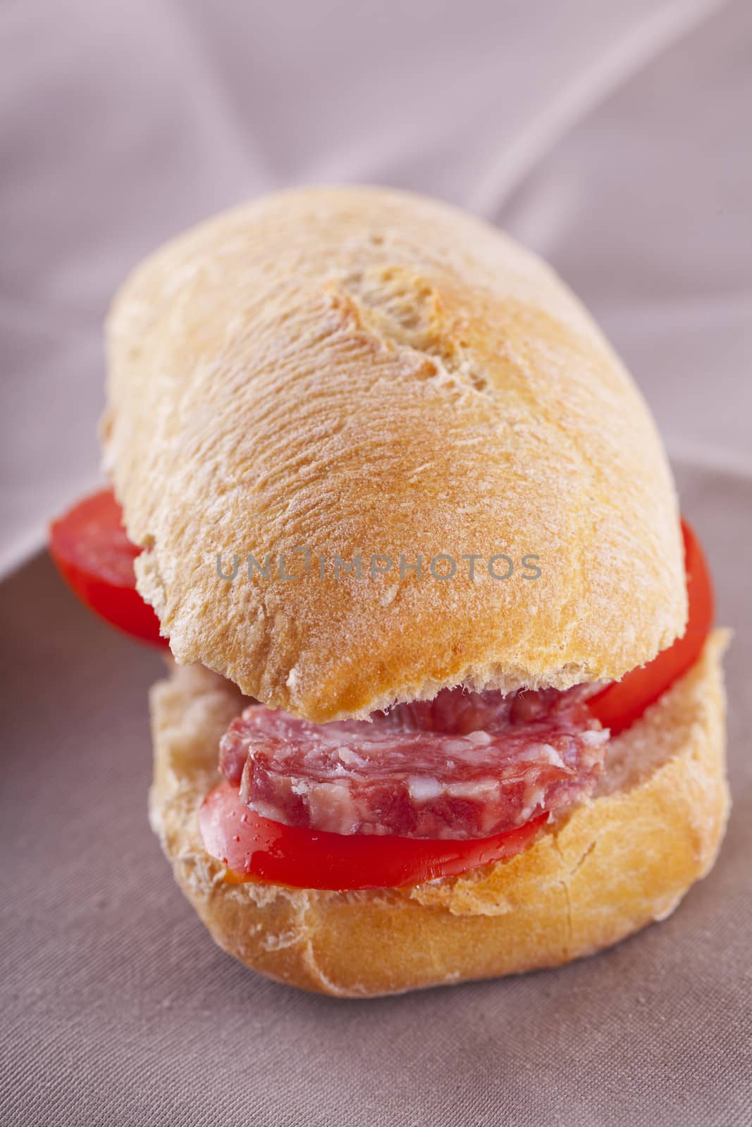 A sandwich with sausage and tomato over brown napkin