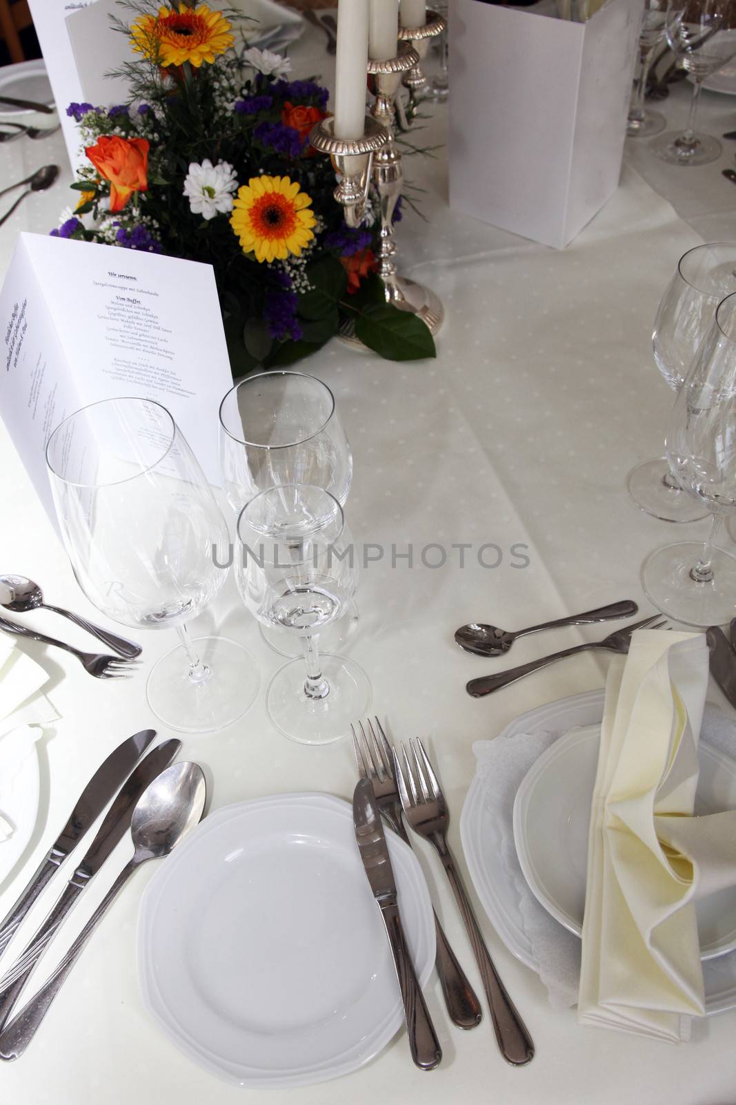 High angle view of a formal table setting at wedding reception or catered event with white linen, silverware, glassware, a menu and floral centrepice