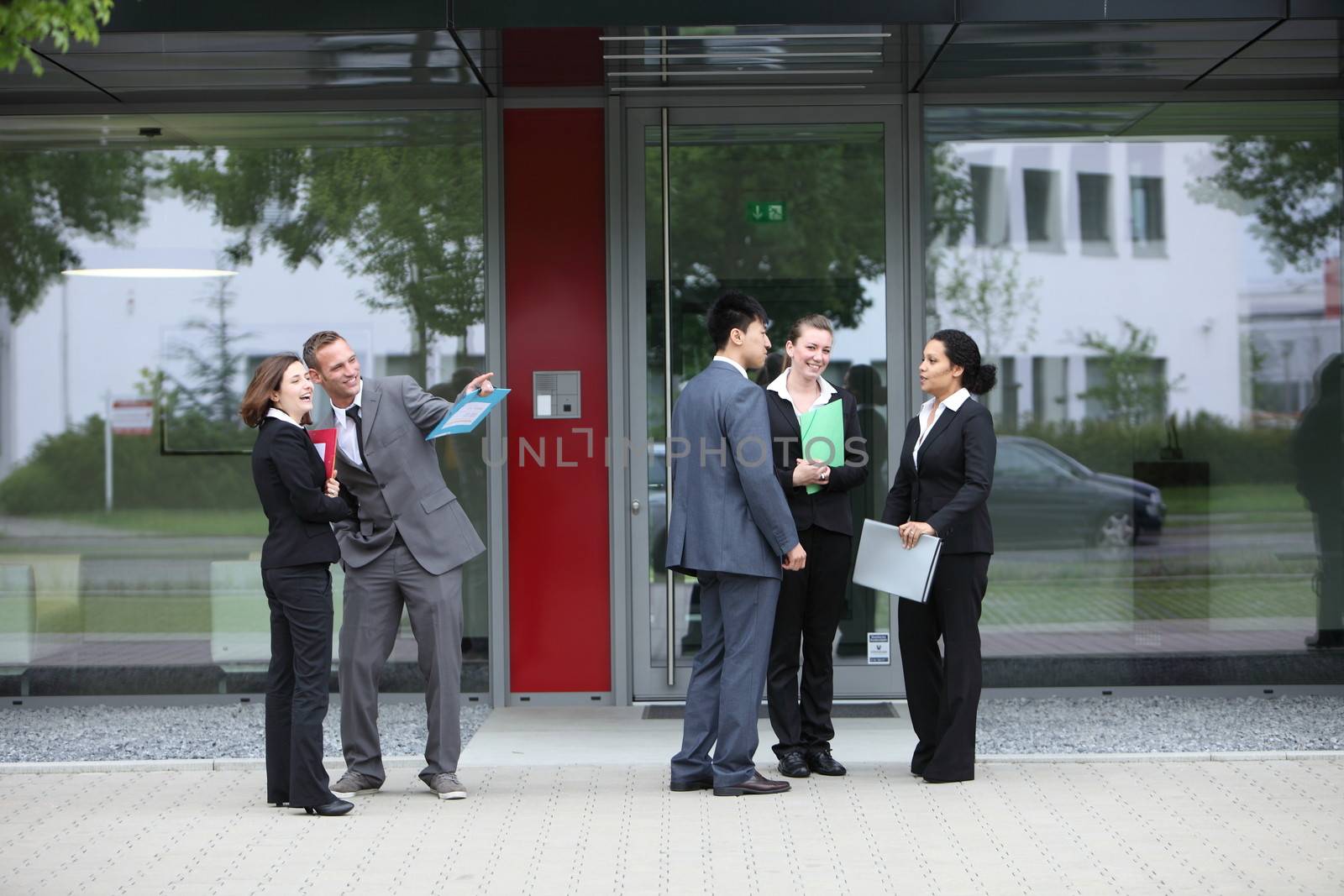 Groups of young diverse businesspeople in suits chatting outdoors in front of the entrance to their office block