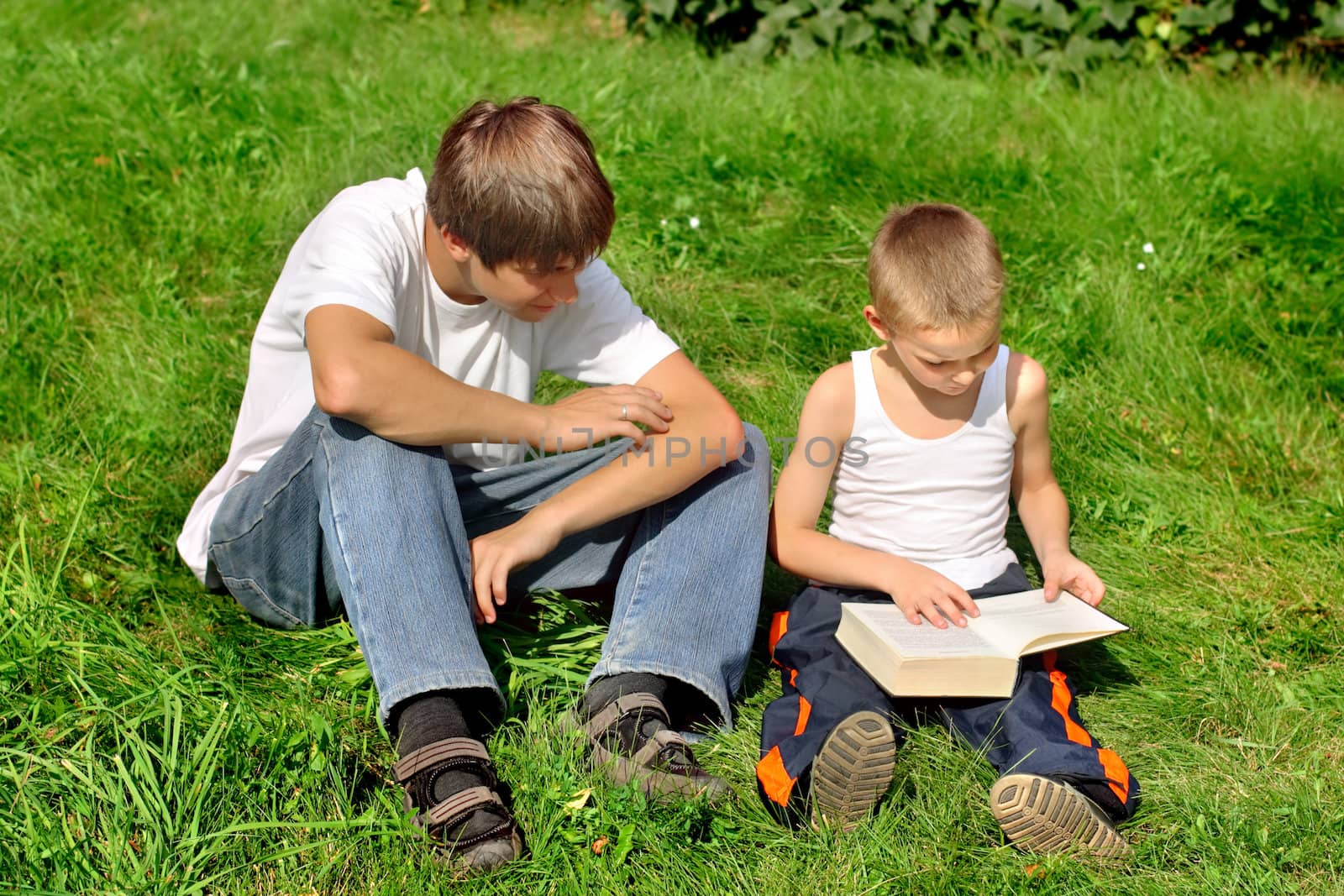 The happy teenager and kid with a book on a summer meadow