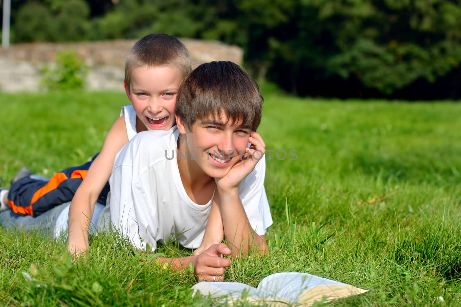 The happy teenager and kid with a book on a summer meadow