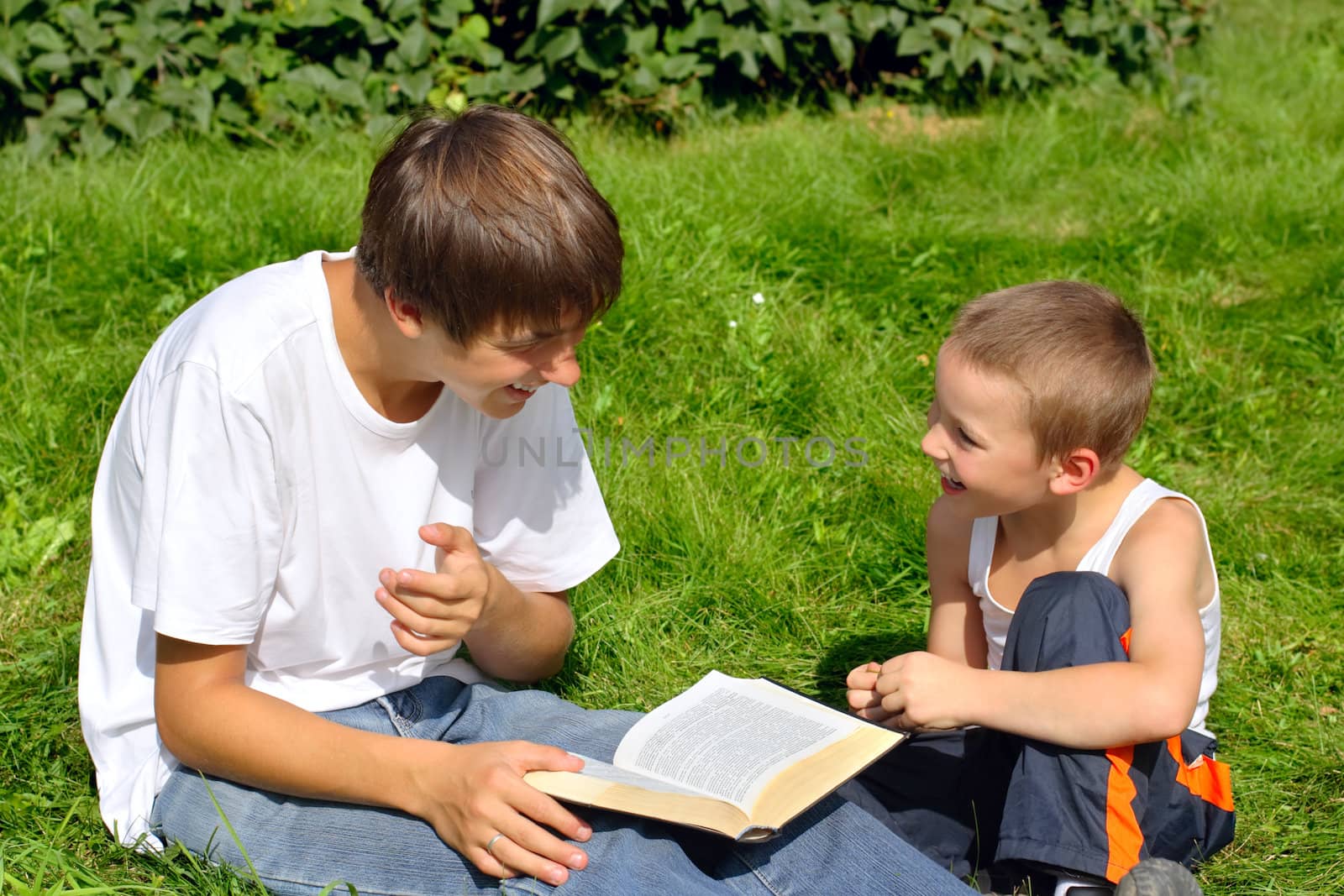 The happy teenager and kid with a book on a summer meadow