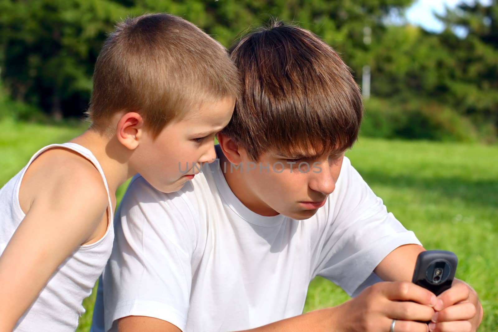 teenager and kid with mobile phone on a summer meadow