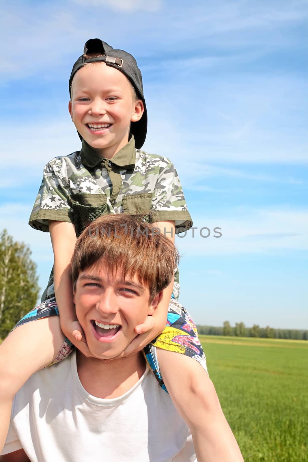 The happy child sits on the teenager shoulders
