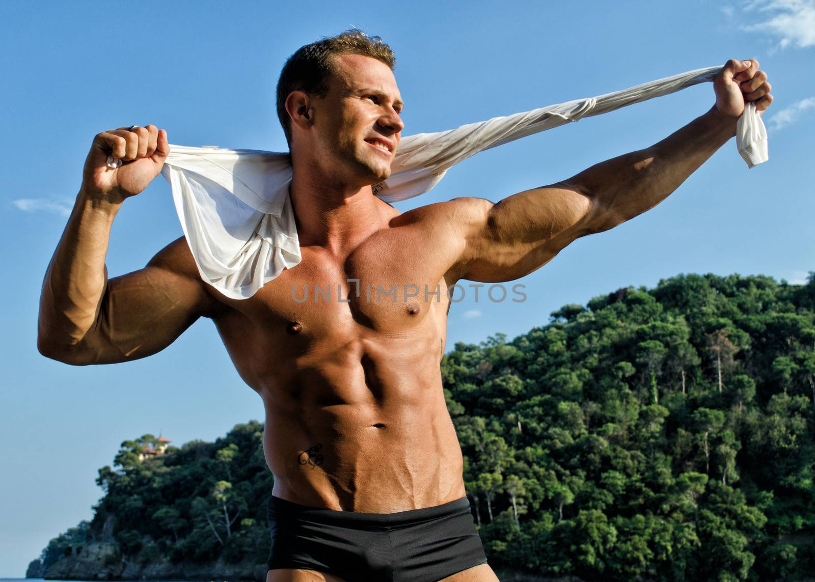 Handsome young bodybuilder with arms open in nature setting by artofphoto