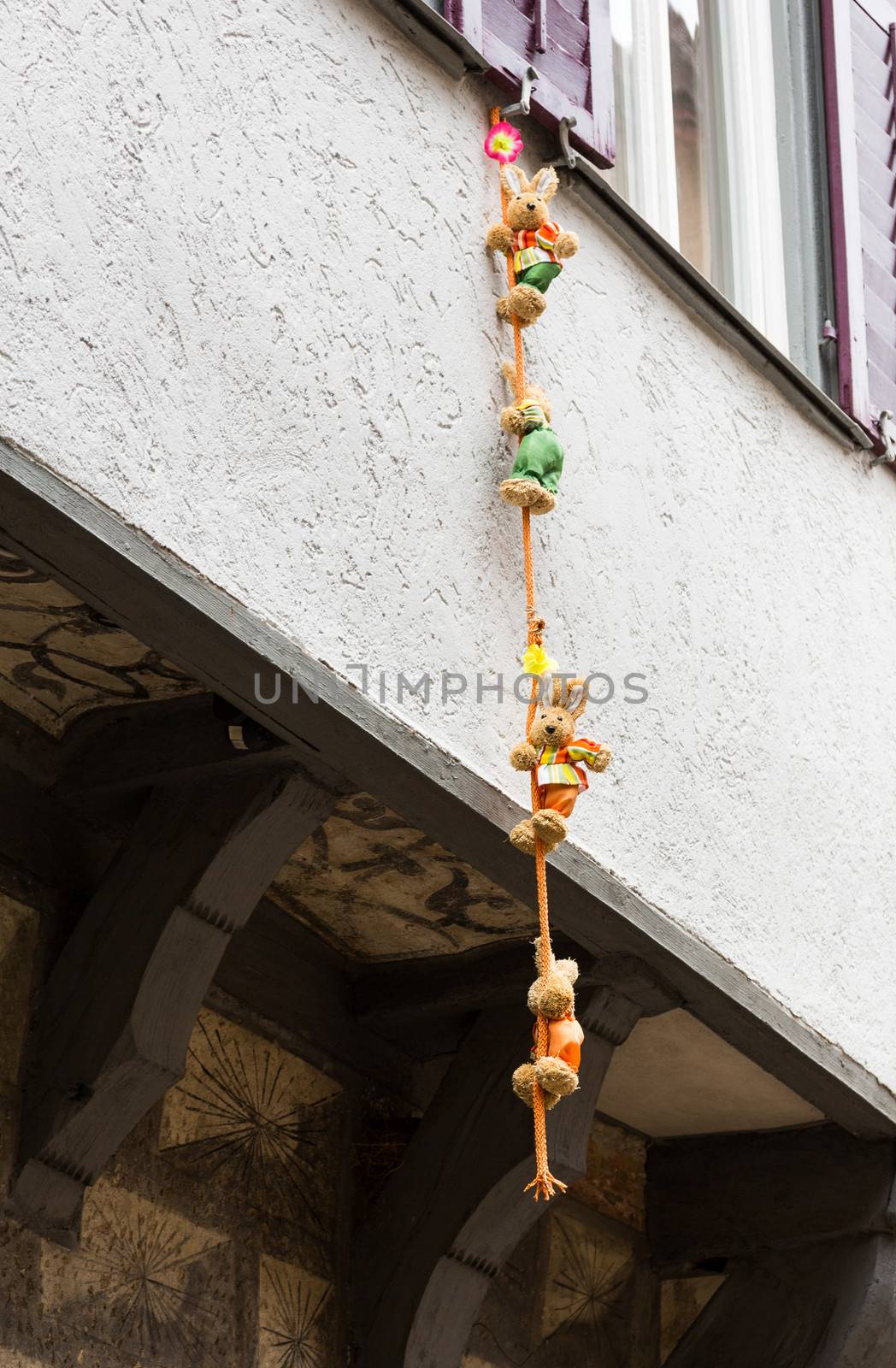 Funny photo of four small stuffed bears and toys climbing down a rope suspended from window of old half-timbered house