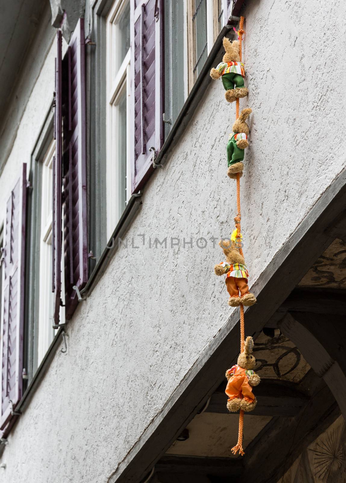 Funny photo of four small stuffed bears and toys climbing down a rope suspended from window of old half-timbered house