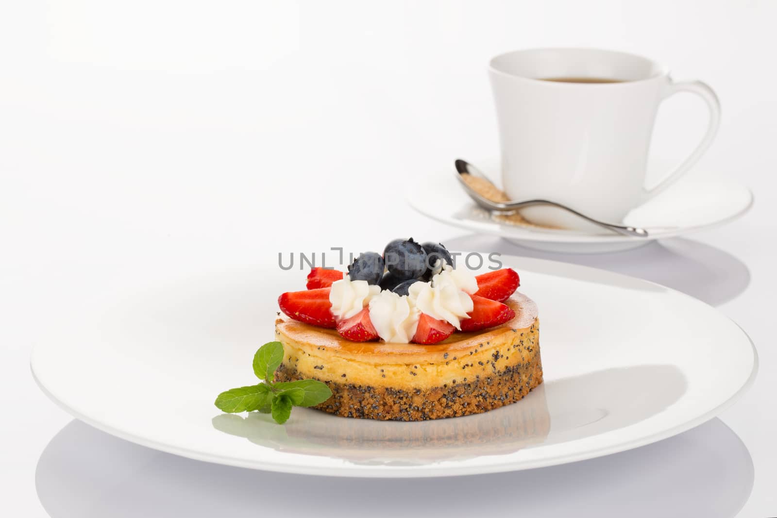 Cheesecake with strawberry, blueberry, mint and cream on white plate with cup of coffee.