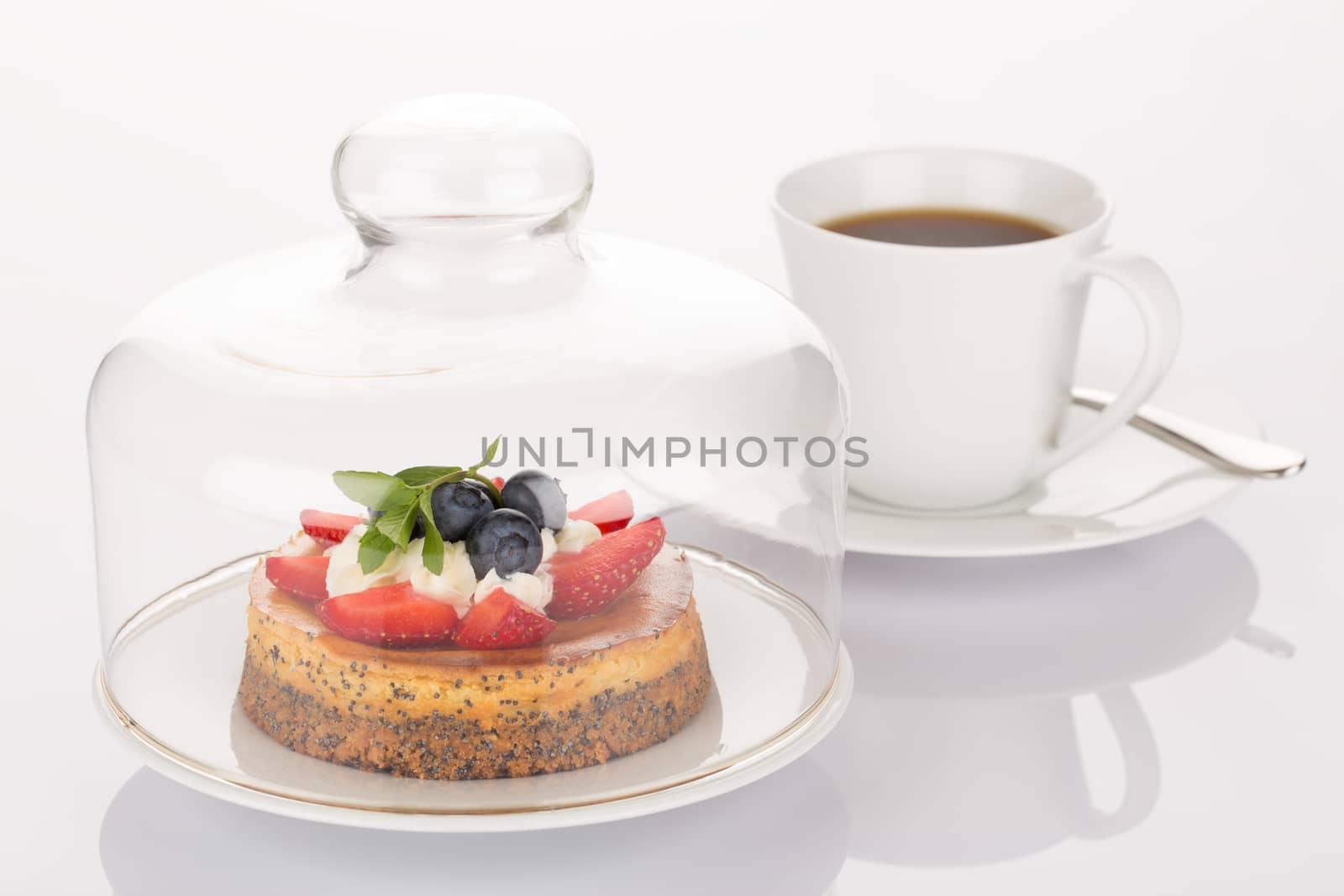 Cheesecake with strawberry, blueberry, mint and cream under glass bell and cup of coffee.