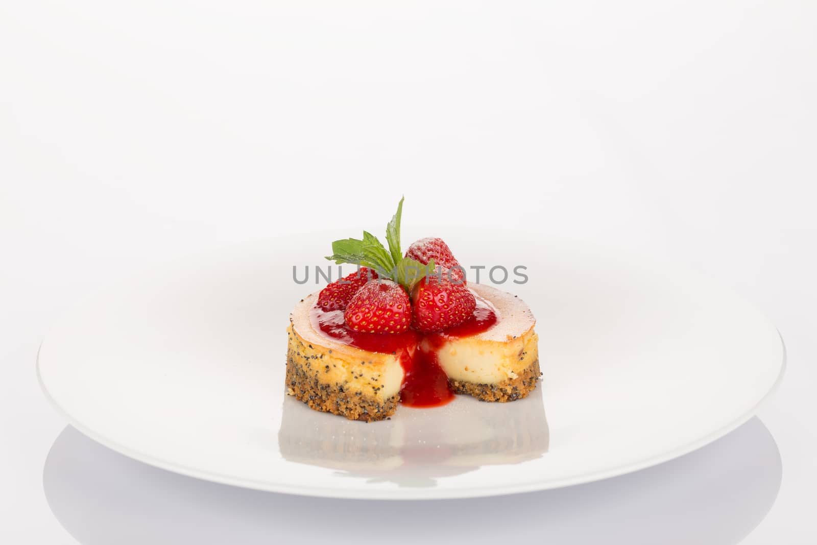 Cheesecake with strawberry, red coulis and mint on white plate.