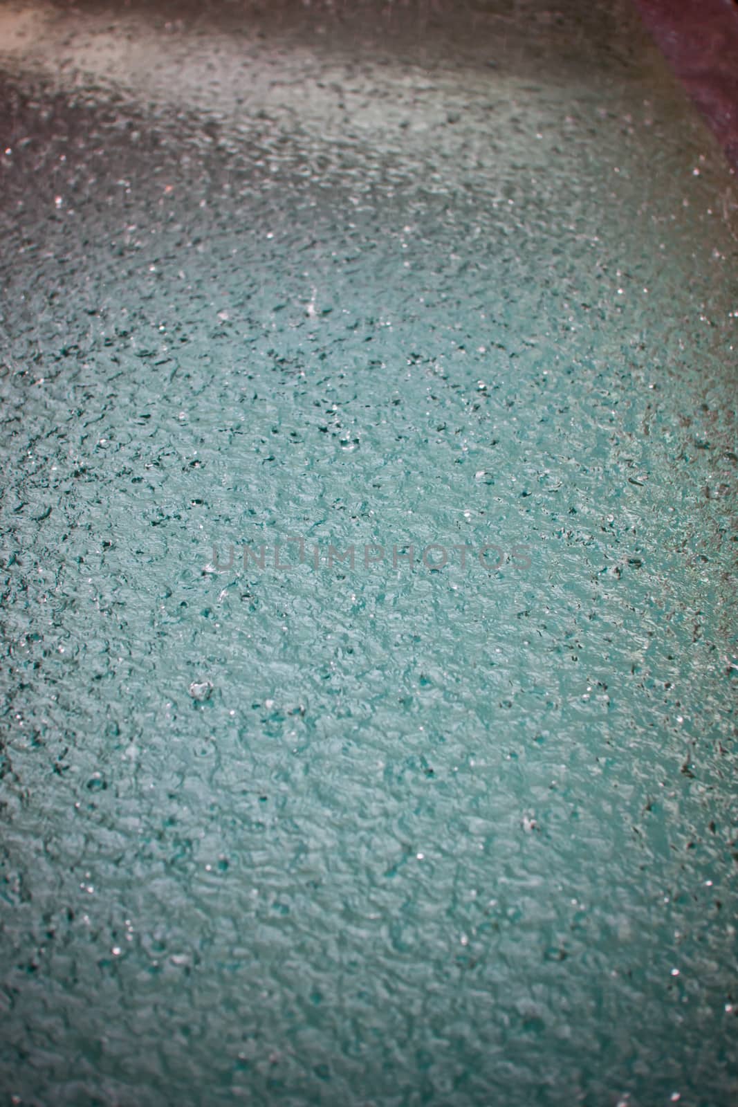 Raindrops falling on the surface of a pool or puddle water creating a textured pattern for a cool natural background