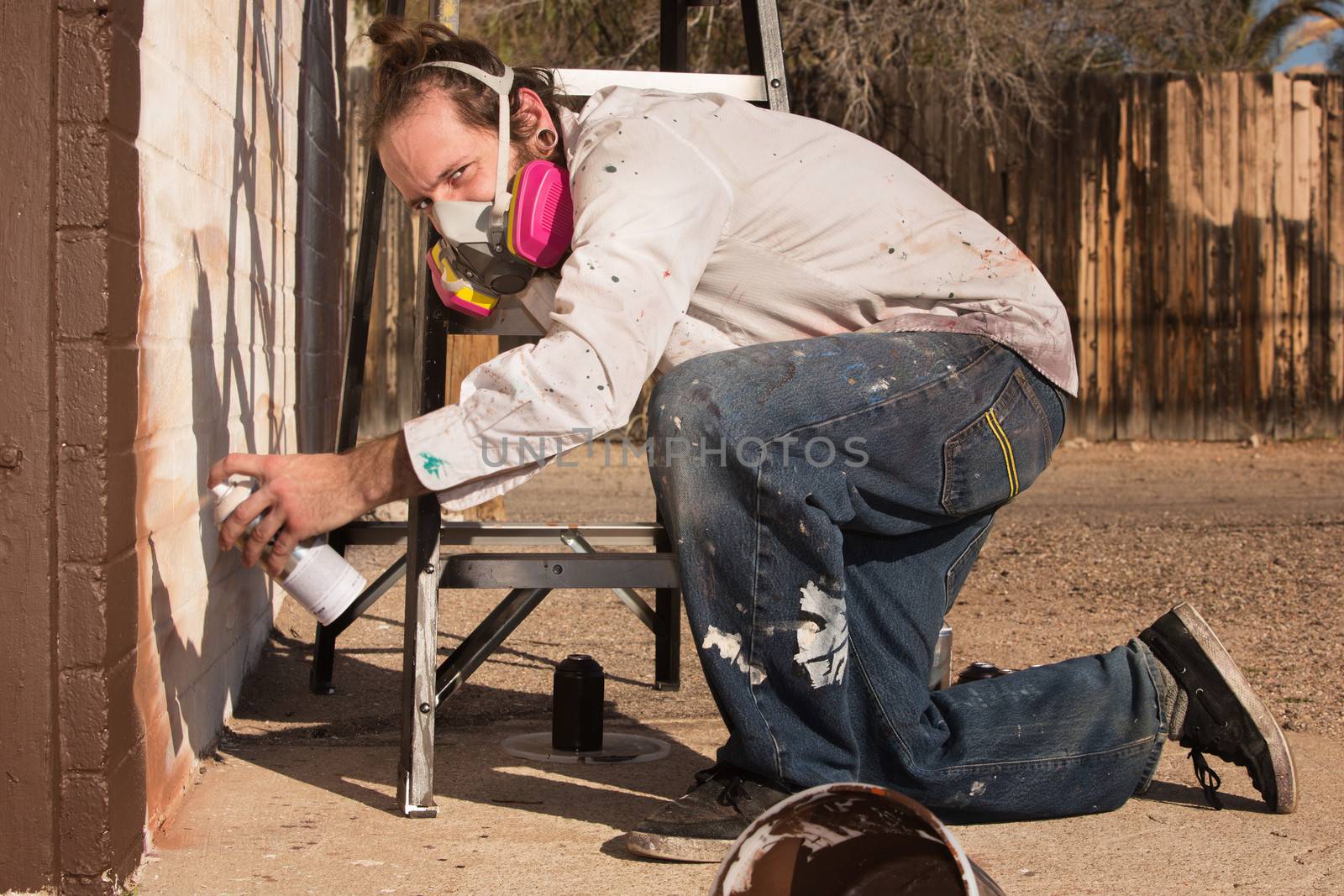 Kneeling graffiti artist with spray paint can and respirator