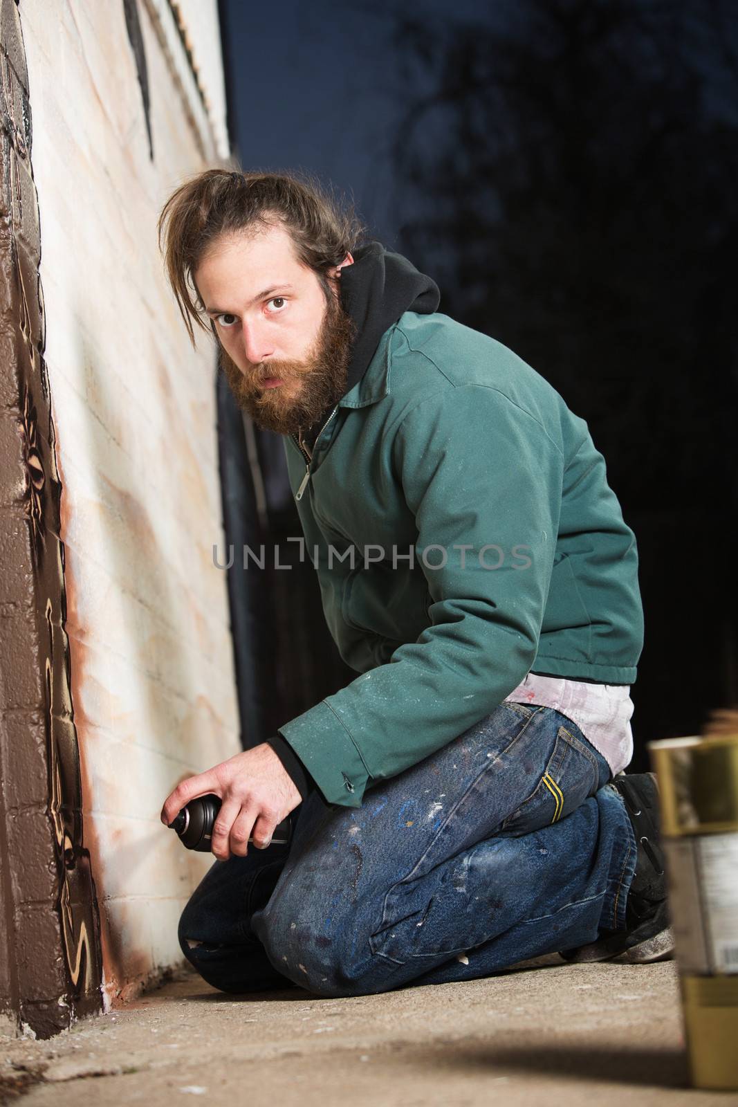 Bearded adult European graffiti artist kneeling on ground