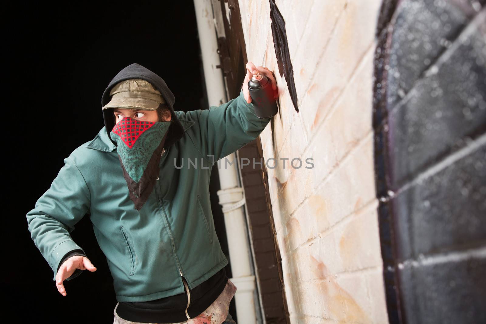 Scared disguised criminal defacing a wall outdoors