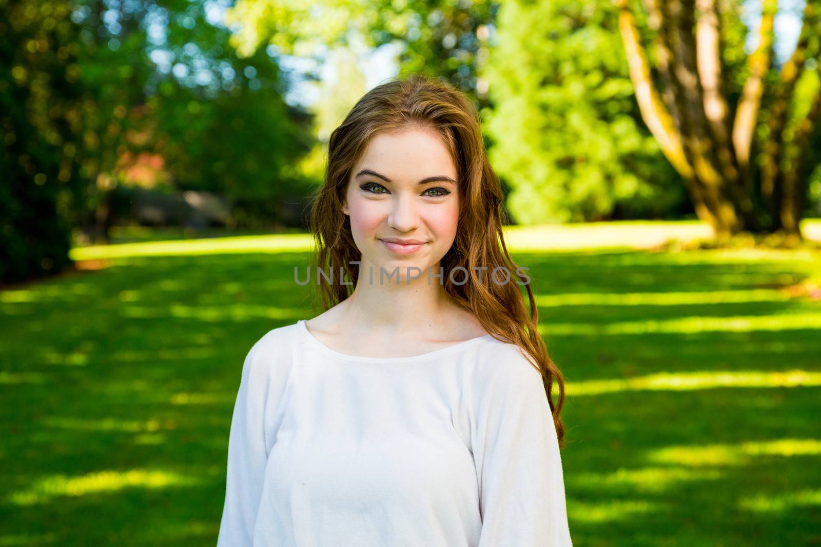 A beautiful young girl poses for a fashion style portrait outdoors at a park with natural lighting.