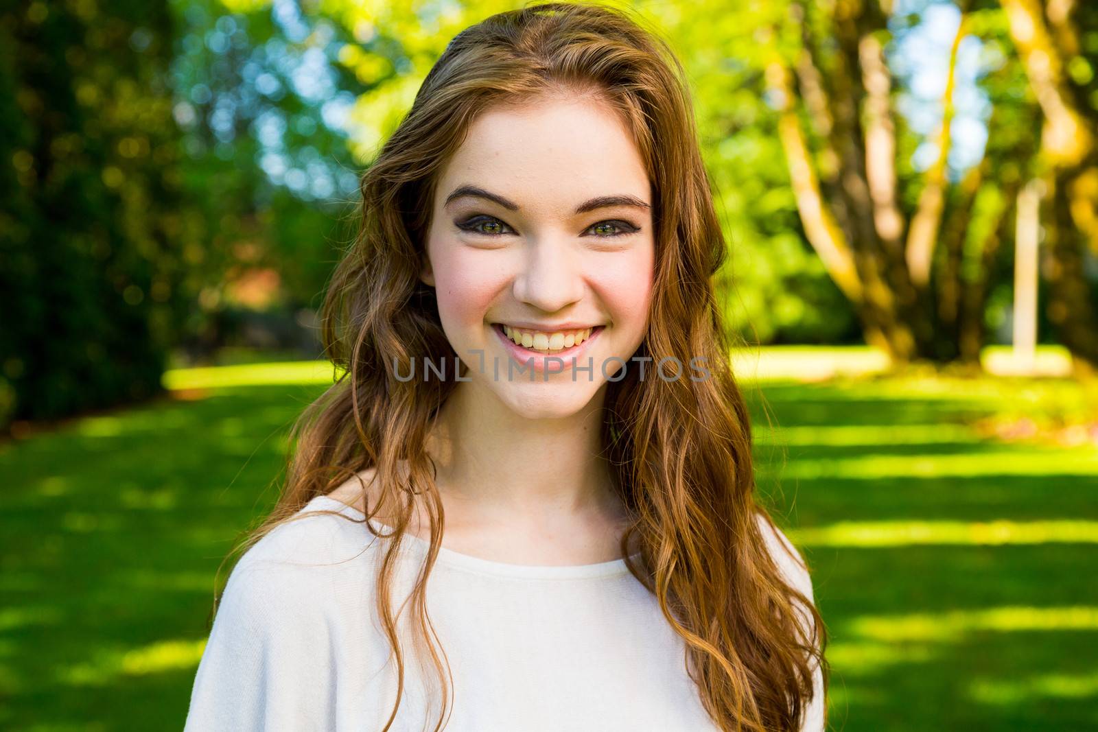 A beautiful young girl poses for a fashion style portrait outdoors at a park with natural lighting.