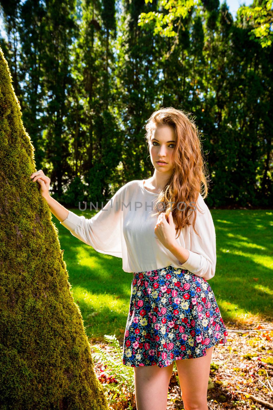 A beautiful young girl poses for a fashion style portrait outdoors at a park with natural lighting.