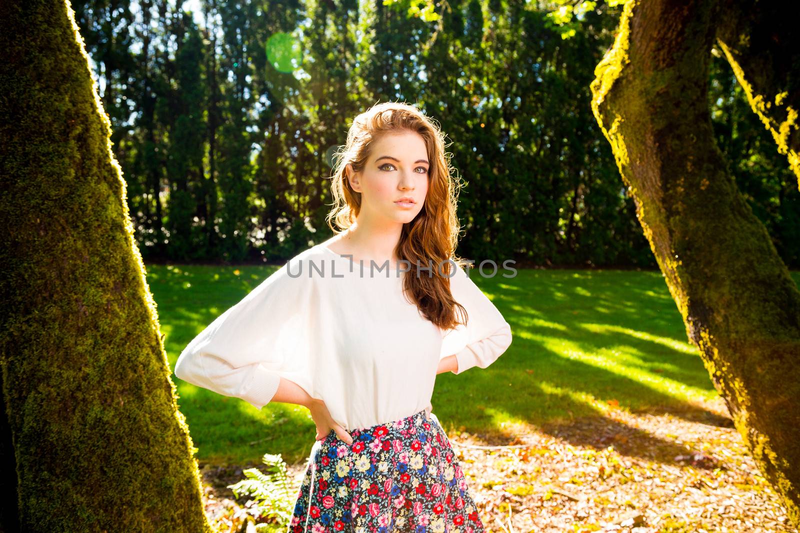 A beautiful young girl poses for a fashion style portrait outdoors at a park with natural lighting.