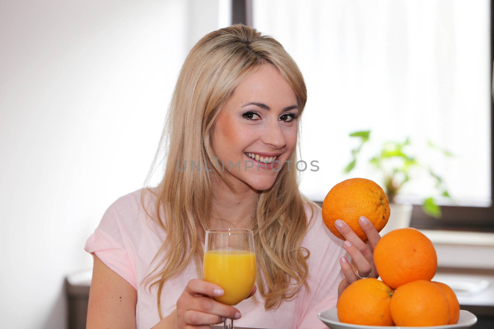Happy young woman with fresh oranges and a glass of orange juice in her hand smiling at the camera conceptual of a healthy diet and lifestyle