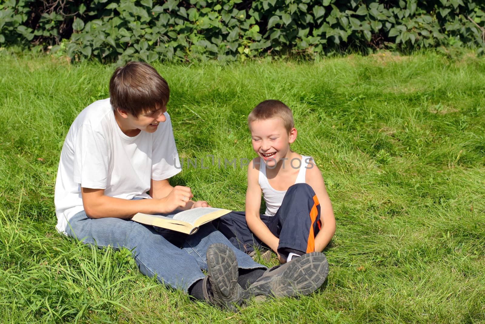 teenager and kid with a book on a summer meadow