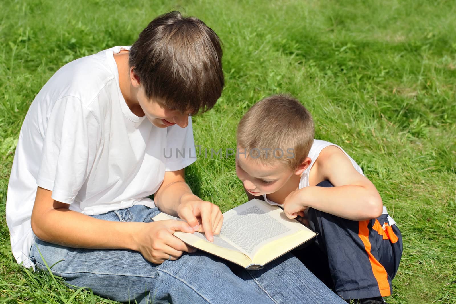 teenager and kid with a book on a summer meadow